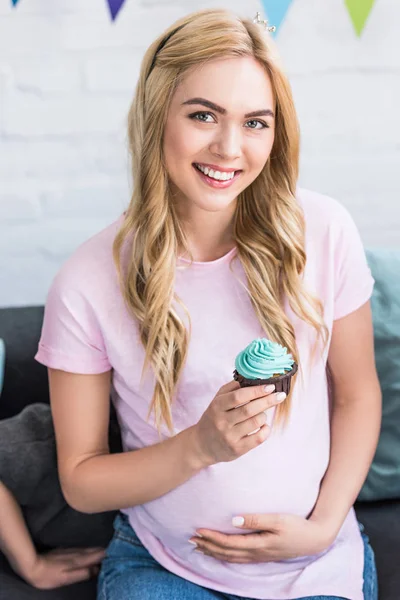 Schöne schwangere Frau mit Cupcake und Blick in die Kamera bei Baby Shower Party — Stockfoto