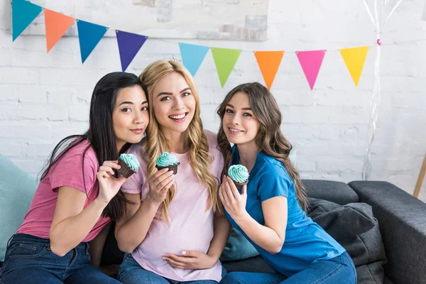 Amigos multiétnicos y mujeres embarazadas con cupcakes en la fiesta del bebé - foto de stock