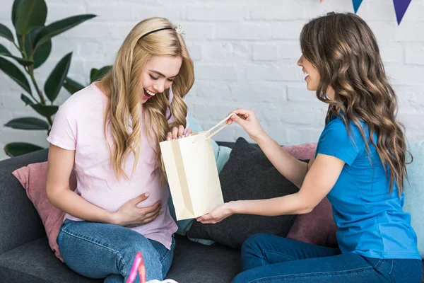 Side view of woman presenting gift to pregnant friend at baby-party — Stock Photo