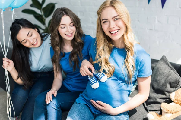 Pregnant woman putting baby shoes on belly at baby shower party — Stock Photo