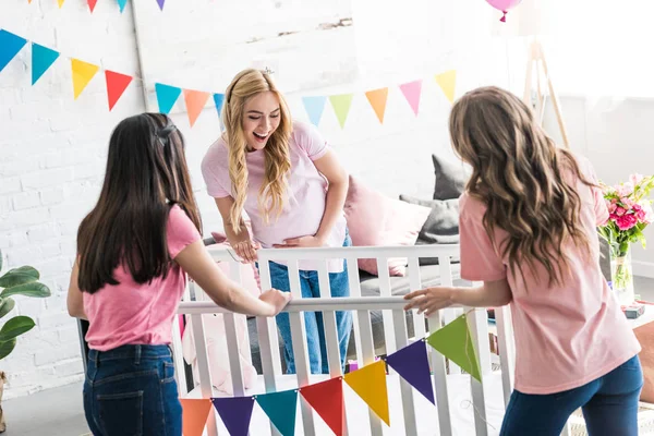 Friends and pregnant woman looking at new crib at baby-party — Stock Photo