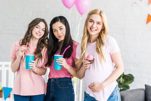 Amigos multiculturales y mujer embarazada con bebidas y cupcake en fiesta de baby shower - foto de stock