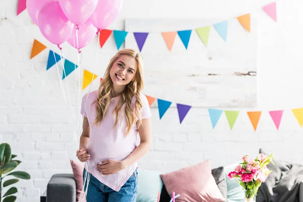 Atractiva mujer embarazada de pie con un paquete de globos y mirando a la cámara en la fiesta del bebé - foto de stock