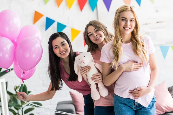 Amici multiculturali sorridenti e donna incinta in posa con coniglio giocattolo a baby-party — Foto stock