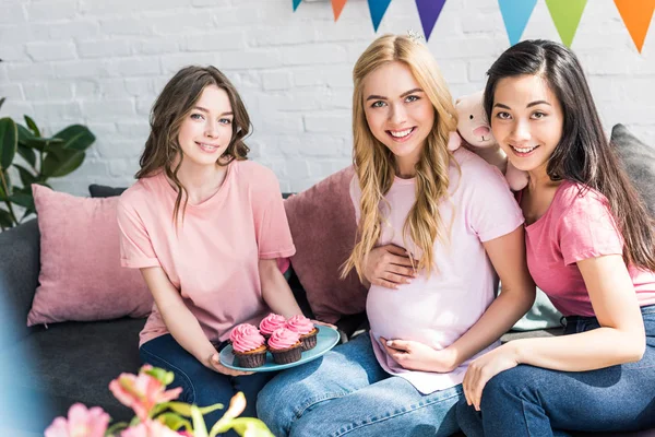 Amigos multiculturales y mujer embarazada con cupcakes rosados en fiesta de la ducha del bebé - foto de stock