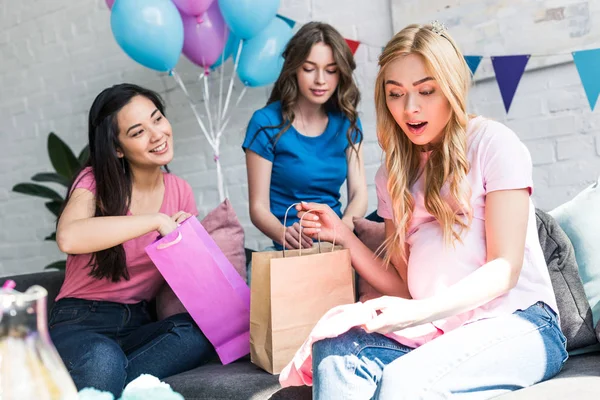 Surprised pregnant woman looking at presents from multicultural friends on baby-party — Stock Photo