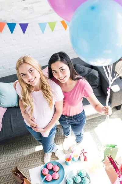 Vista de ángulo alto de amigos multiculturales sosteniendo un paquete de globos en la fiesta del bebé - foto de stock