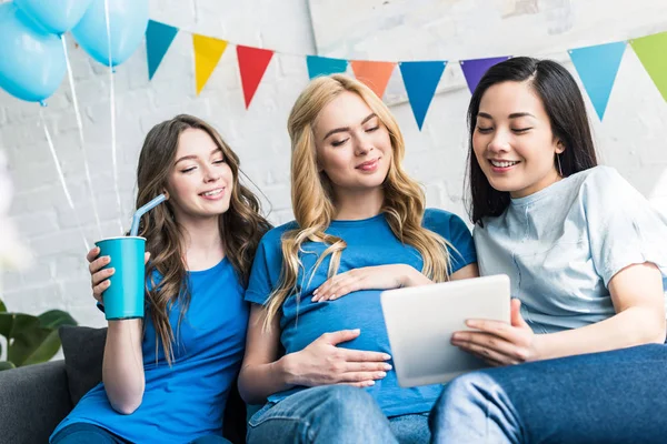 Amigos multiculturales y mujeres embarazadas usando tableta en fiesta de la ducha del bebé - foto de stock