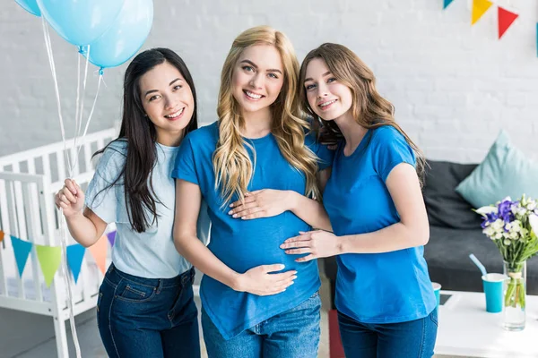 Sonrientes amigos multiétnicos con globos y mujer embarazada mirando a la cámara en la fiesta del bebé - foto de stock