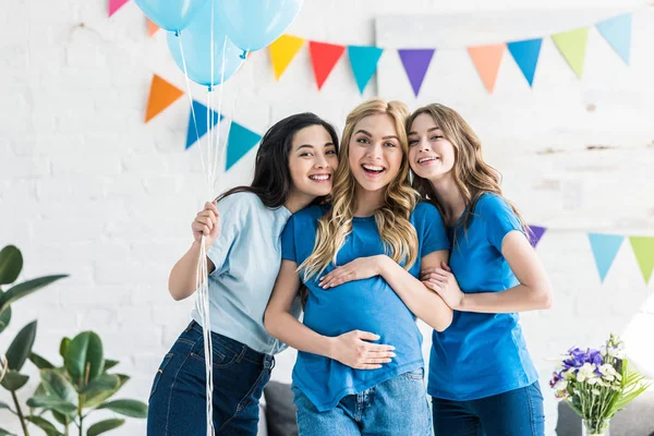 Amigos multiculturais sorridentes com balões e mulher grávida olhando para a câmera na festa do bebê — Fotografia de Stock