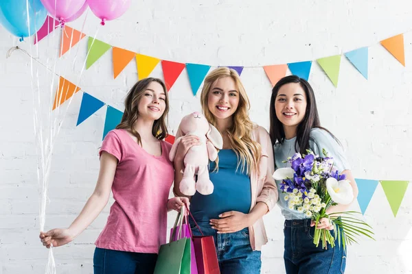 Amigos multiculturales felices y mujer embarazada de pie con regalos en la fiesta del bebé - foto de stock