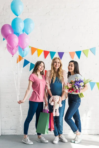 Sonrientes amigos multiétnicos y mujeres embarazadas de pie con regalos en la fiesta del bebé - foto de stock