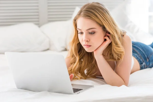 Belle jeune femme en utilisant un ordinateur portable sur le lit — Photo de stock