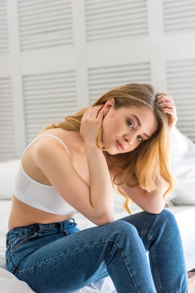 Schönes Mädchen in Jeans und weißem BH auf dem Bett sitzend — Stockfoto
