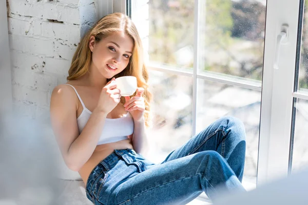 Menina bonita feliz sentado no peitoril da janela com xícara de café — Fotografia de Stock