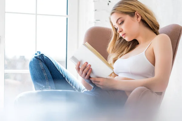 Loira linda menina ler livro e sentado em poltrona — Fotografia de Stock