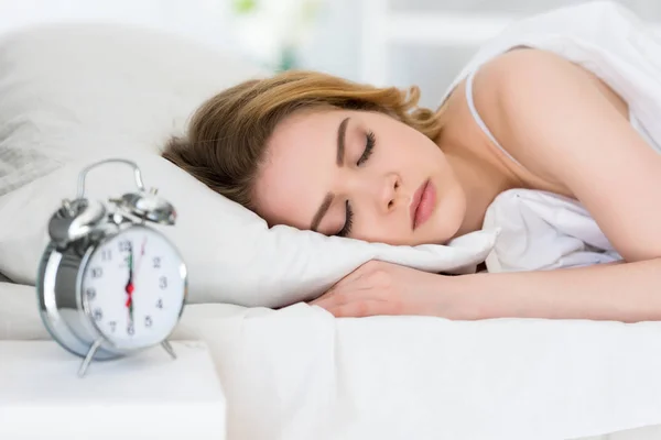 Selektiver Fokus der jungen Frau, die mit Wecker im Bett schläft — Stockfoto