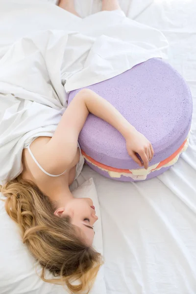 Top view of beautiful girl sleeping with big purple macaron on bed — Stock Photo