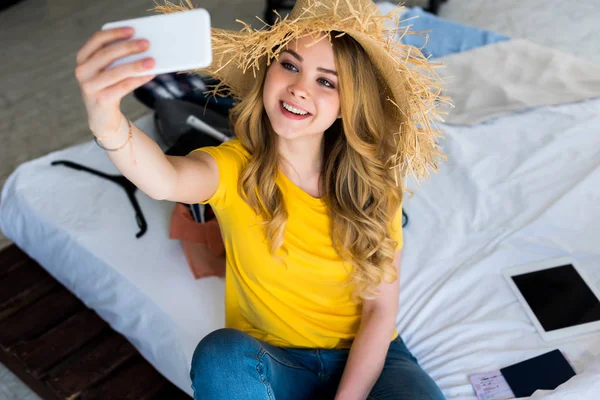 Atractiva chica sonriente en sombrero de paja tomando selfie en el teléfono inteligente - foto de stock