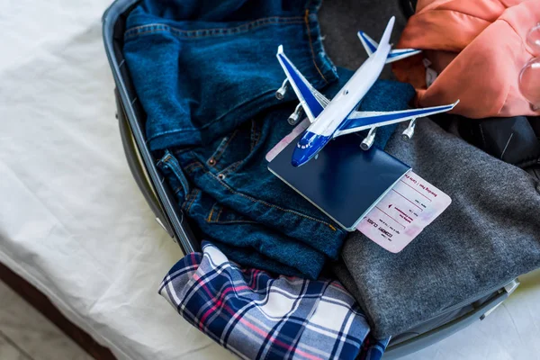 Fermer la valise avec vêtements, passeport, billet d'avion et modèle d'avion — Photo de stock