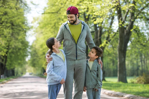 Smiling father embracing daughter and son in park — Stock Photo