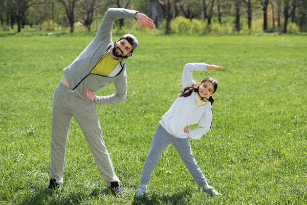 Hija y padre haciendo ejercicio físico sobre hierba - foto de stock