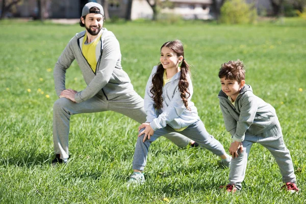 Отец с дочерью и сыном занимаются физическими упражнениями на травянистом лугу в парке — стоковое фото