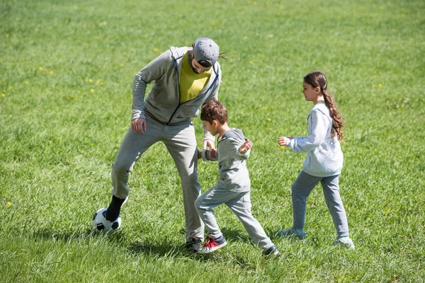 Отец играет в футбол с дочерью и сыном в парке — стоковое фото