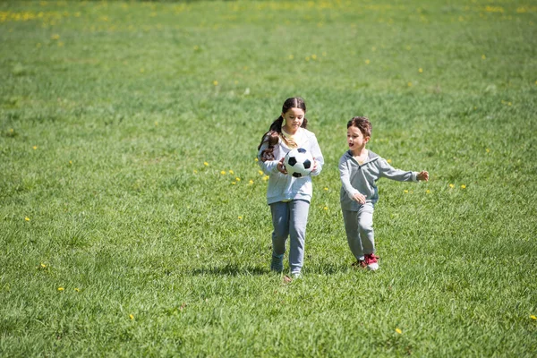 Брат и сестра играют в футбол на травянистом лугу — стоковое фото
