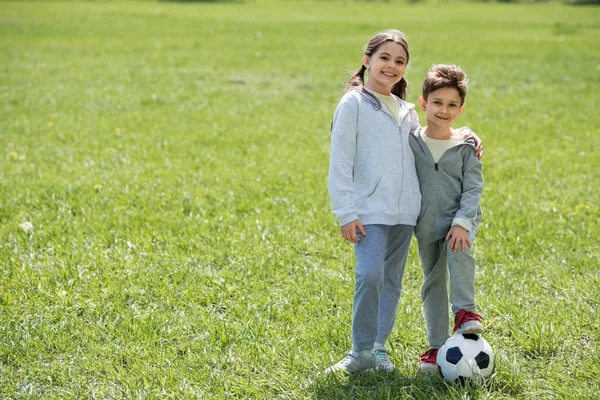 Щасливий брат і сестра з м'ячем, що стоїть на трав'янистих лугах — стокове фото