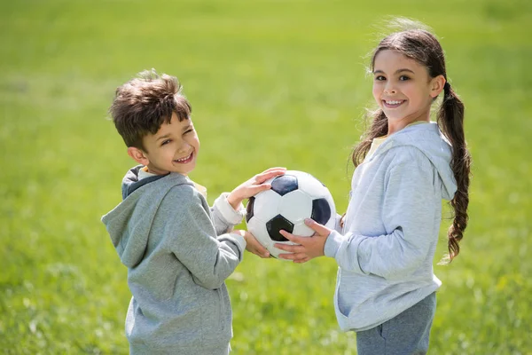 Lächelndes Geschwisterpaar hält Ball auf Wiese — Stockfoto