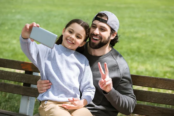 Hija tomando selfie con padre haciendo gesto de paz en el parque - foto de stock