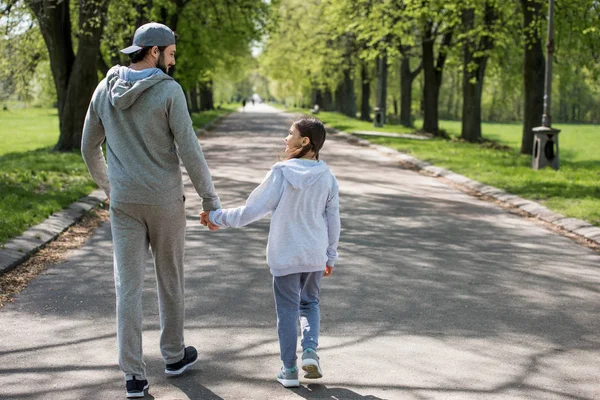 Visão traseira do pai e da filha de mãos dadas e caminhando no caminho no parque — Fotografia de Stock
