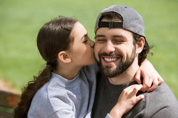 Pequena filha beijando sorrindo pai no banco no parque — Fotografia de Stock