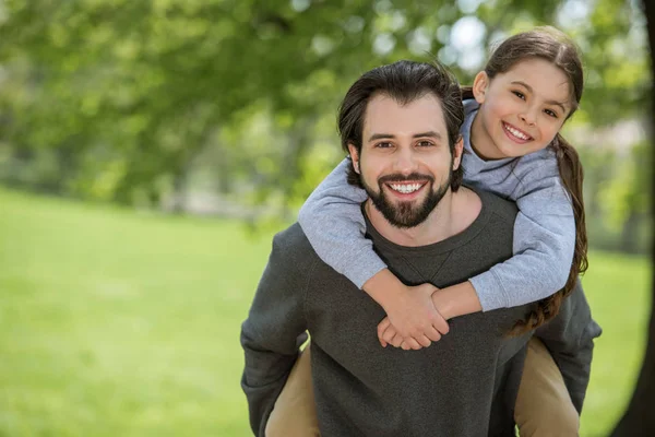 Smiling father doing piggyback ride to daughter in park — Stock Photo