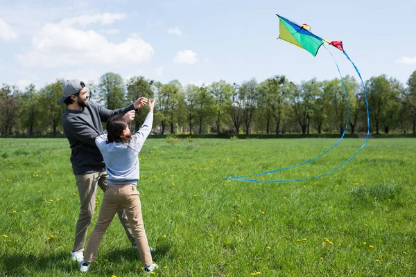Smiling father and daughter flying kite on meadow in park — Stock Photo