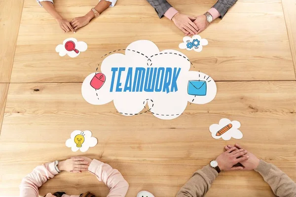 Overhead view of multiracial business people at wooden table with blank paper clouds, teamwork inscription — Stock Photo