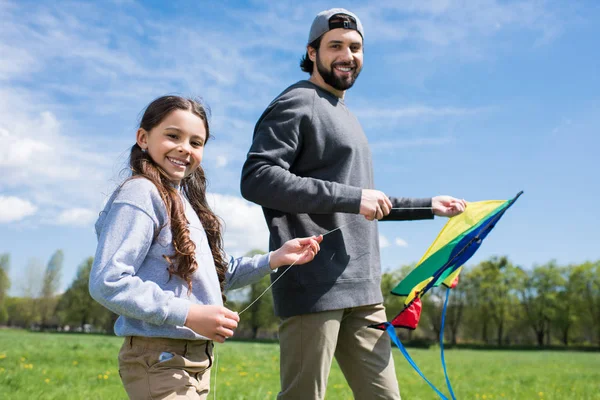 Дочь с отцом держит воздушного змея на лугу в парке — стоковое фото