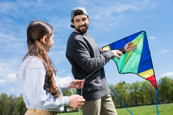 Padre e hija sosteniendo cometa en prado en parque - foto de stock