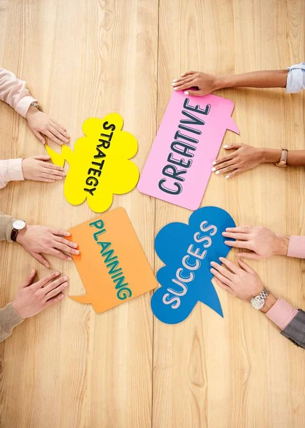 Overhead view of multiracial business people at wooden table with colorful chat bubbles with strategy, planning, creative, success signs — Stock Photo