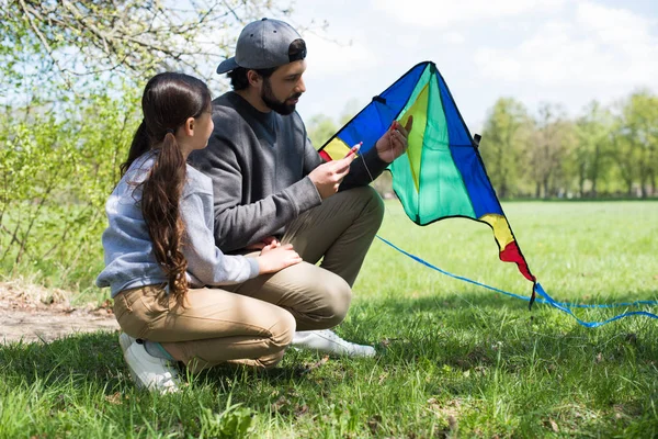 Side view of father and daughter sitting with kite on meadow — Stock Photo