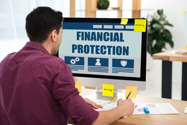 Vue partielle de l'homme d'affaires travaillant sur ordinateur avec inscription de protection financière à l'écran sur le lieu de travail dans le bureau — Photo de stock