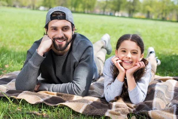 Sonriente hija y padre acostado a cuadros en el parque - foto de stock
