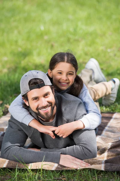 Sorrindo filha deitado no pai de volta no parque — Fotografia de Stock