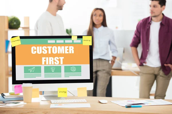 Selective focus of customer first inscription on computer screen and multiethnic business colleagues in office — Stock Photo