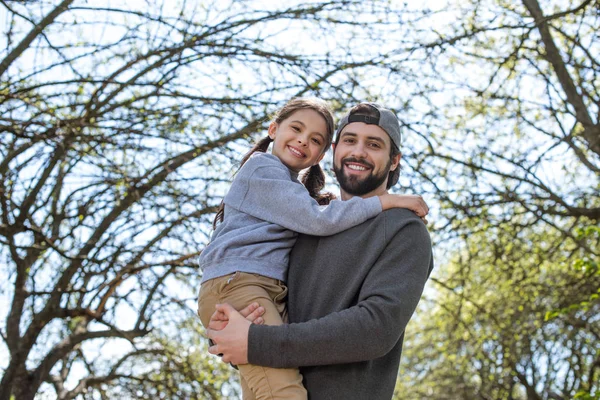 Low angle view of smiling father holding daughter in park — Stock Photo