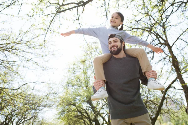 Low angle view of daughter sitting on father shoulders in park — Stock Photo