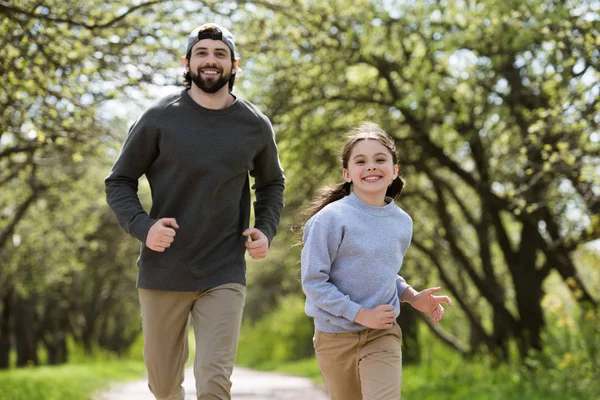 Sonrientes padre e hija corriendo en el parque - foto de stock