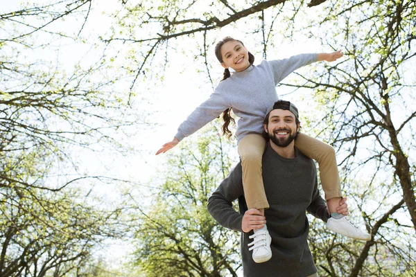 Low angle view of daughter sitting on father shoulders in park — Stock Photo