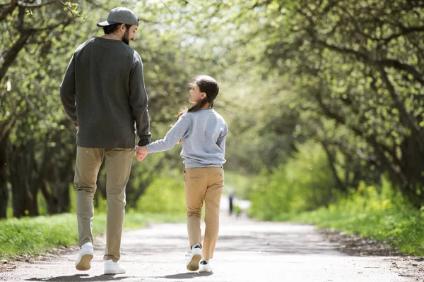Visão traseira do pai e da filha andando e de mãos dadas no parque — Fotografia de Stock